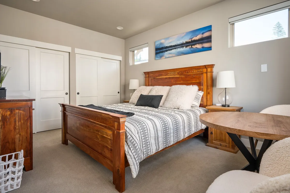 A bedroom featuring a wooden bed frame with decorative bedding, a side table with a lamp, and artwork on the wall. The space is filled with soft natural light, evoking a serene and restful atmosphere perfect for unwinding after a day of adventure.