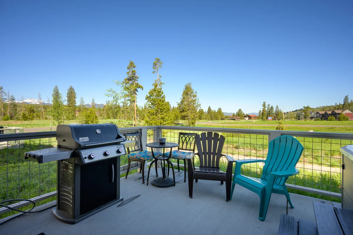 An inviting exterior view of a patio with a grill, dining table, and chairs set against a scenic mountain backdrop. The space is ideal for family barbecues, relaxing after a day of adventures, and soaking in sunset views.