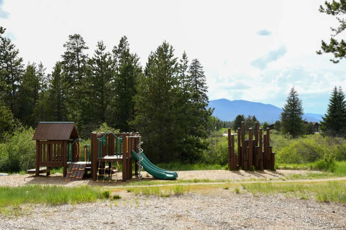 A lively playground structure with a slide and climbing wall is surrounded by greenery, inviting children and families to play and explore. The setting suggests a family-friendly and adventurous atmosphere just steps from the patio.