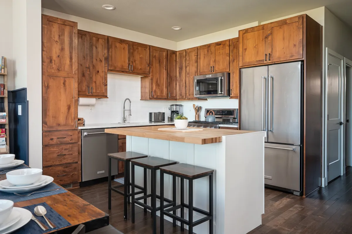 A sophisticated kitchen featuring a large island countertop with bar stools, premium stainless steel appliances, and beautiful wooden cabinetry. The island provides space for meal prep, seating for casual conversation, and ample room for culinary creativity.