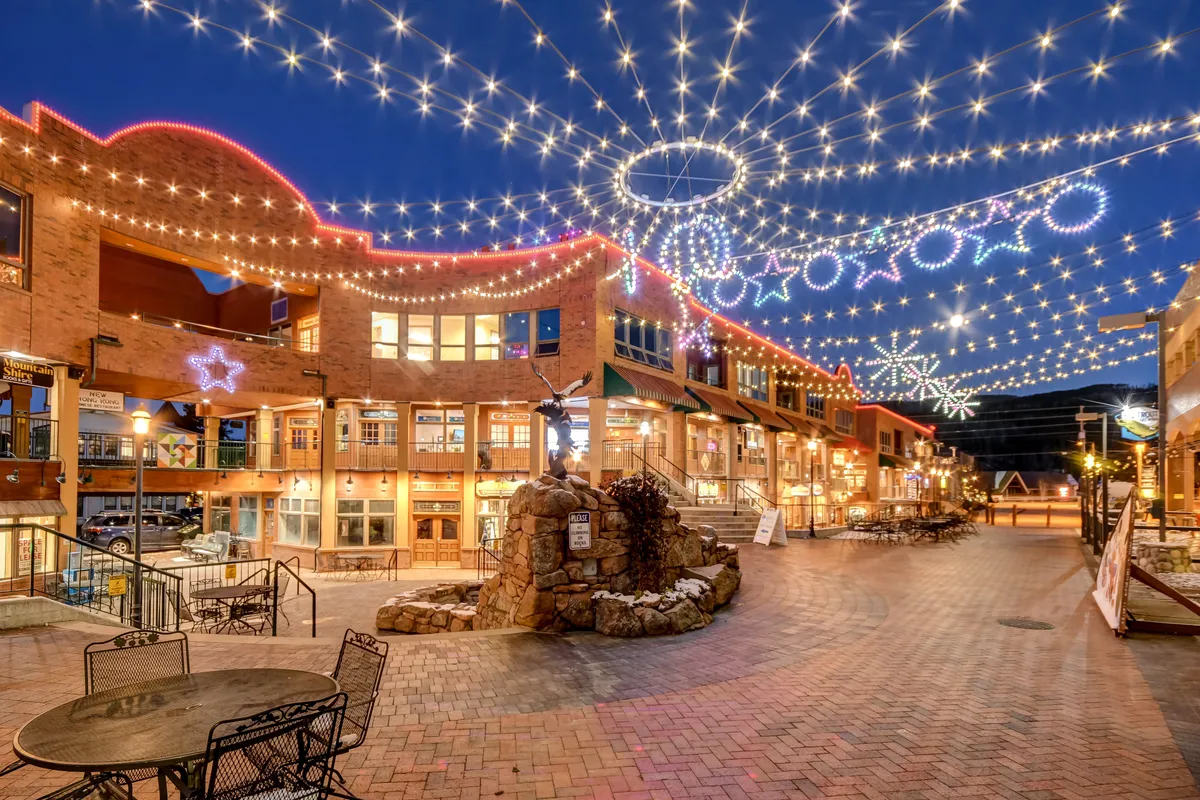 A lively exterior setting with decorative lights strung above a stone fountain and a comfortable seating area, evoking the ambiance of downtown Winter Park's social scene. The image hints at vibrant family outings, shopping, and dining experiences.