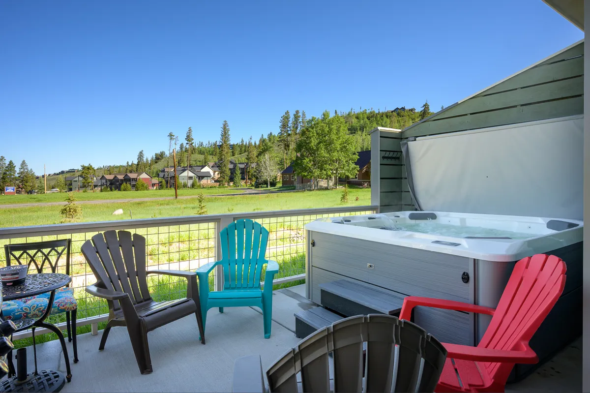 The photo highlights a hot tub and a collection of colorful chairs on a patio, looking out toward a scenic landscape. The scene is designed for both relaxation and casual gatherings, with hints of sunset and stargazing potential.
